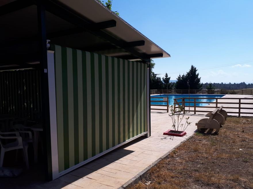 Toldo vertical de rayas verdes en un porche junto a una piscina