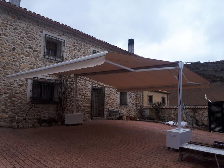 Toldo beige de brazos en la fachada de una casa de piedra