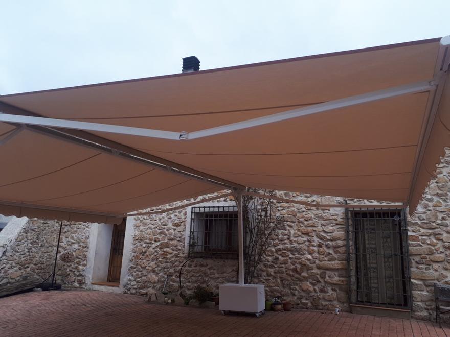 Toldo beige de gran tamaño ante una casa de piedra