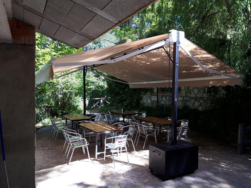 Toldo beige con estructura propia sobre una terraza con mesas